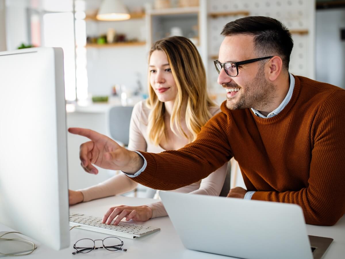 Eine junge Frau und ein etwas älterer Mann sitzen zusammen an einem Computer. Er zeigt auf etwas auf dem Bildschirm.