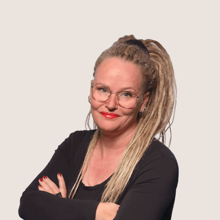 Lächelnde Frau mit einem großen blonden Pferdeschwanz und einer runden Brille.
