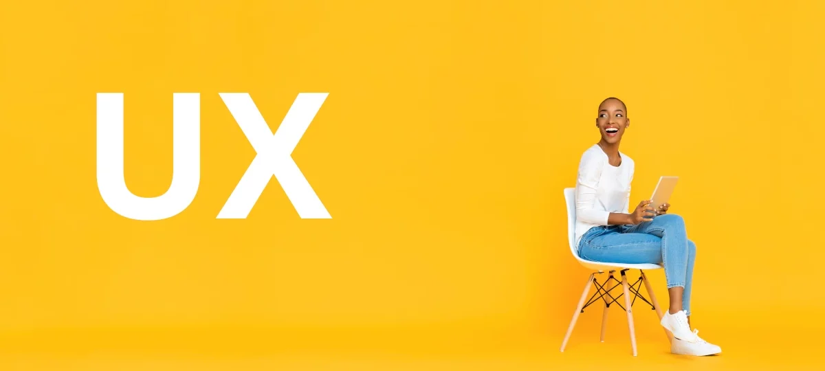 Frau sitzt lächelnd auf einem Stuhl mit einem Tablet in der Hand vor einem gelben Hintergrund, neben dem groß die Buchstaben 'UX' stehen. Symbolisiert Nutzerfreundlichkeit und modernes Design.